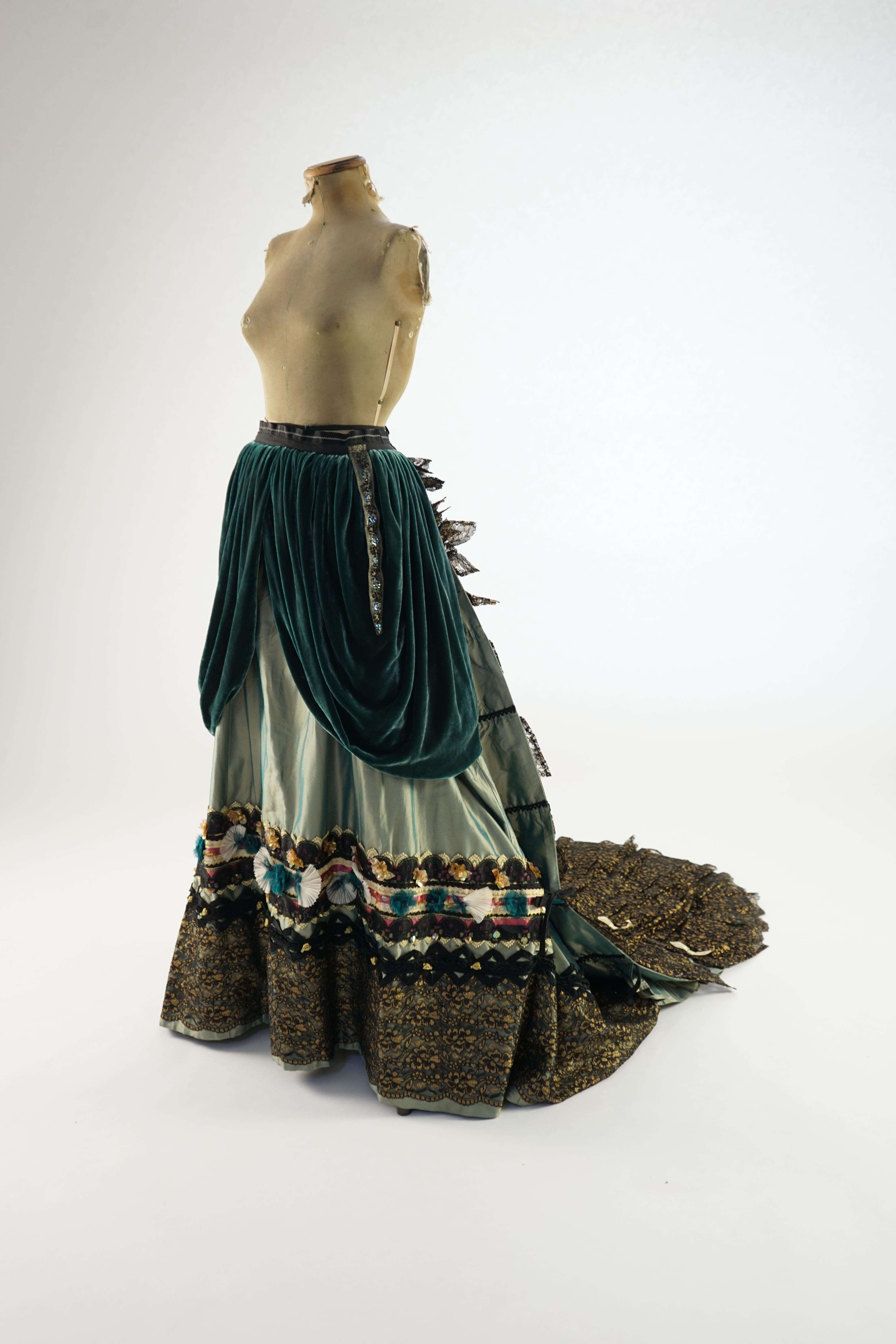 An Edwardian style lady's green taffeta skirt decorated with beaded, sequinned, ribboned border and swags of silk velvet, together with matching train layered with frilled black and gold lace, appliquéd with gold bows